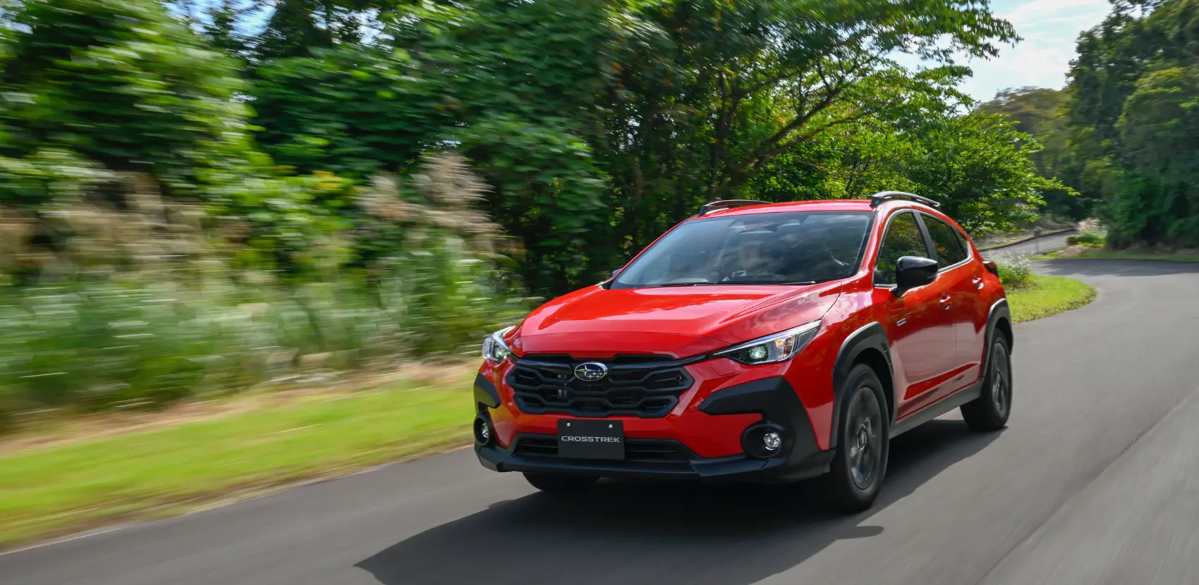Modelo Subaru Crosstrek, color rojo, en carretera con árboles de fondo.