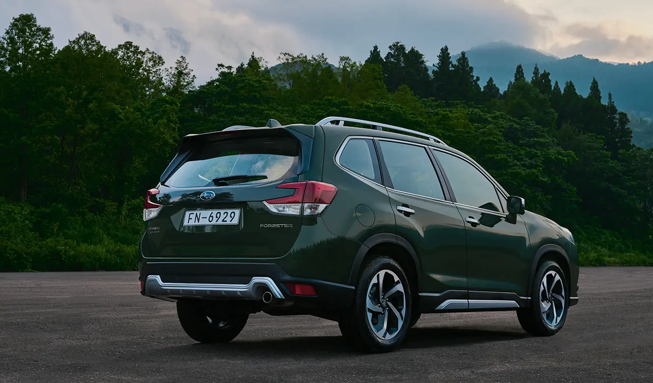 Modelo Subaru Forester SUV híbrida estacionada en terreno arenoso con árboles y montañas de fondo.
