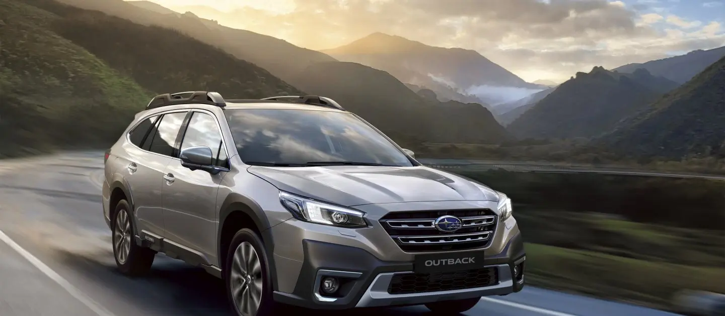 Subaru Outback a velocidad en carretera con montañas y vegetación de fondo.