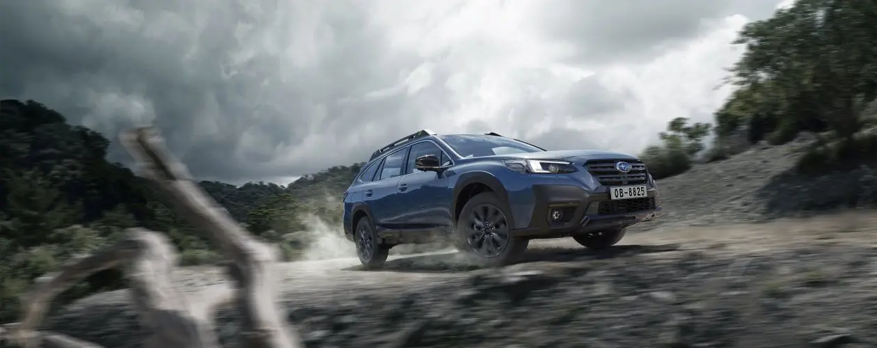 Subaru Outback color azul, en terreno empedrado con vegetación de fondo.